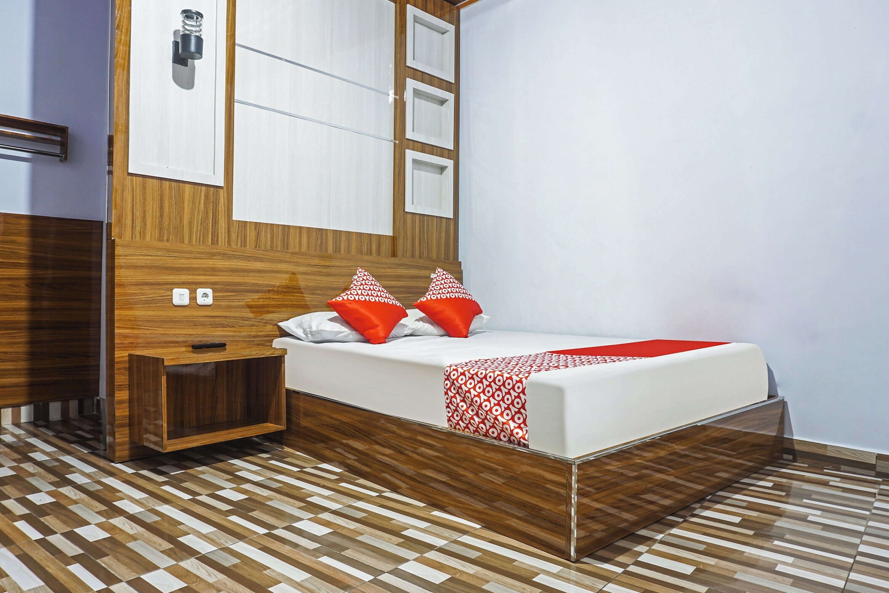 A modern bedroom with a wooden headboard, a bed with red and white patterned pillows, and a checkered floor.