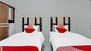 Ein Hotelzimmer mit zwei Betten, jeweils mit einer roten und weißen Bettdecke und passenden Kissen. Im Zimmer befindet sich ein Holzschrank und eine weiße Tür.