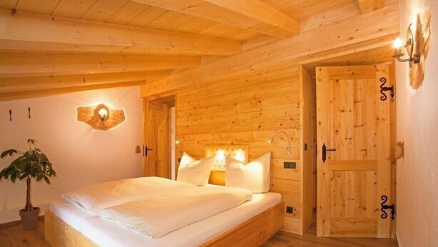 A wooden bedroom with a bed, a wall-mounted light, and a door. - Ferienwohnung Chiemsee (Bernau am Chiemsee)