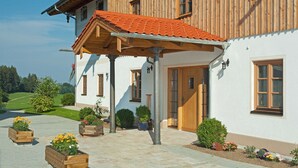 A wooden house with a tiled roof, a covered porch, and a garden with flower beds. - Ferienwohnung Chiemsee (Bernau am Chiemsee)