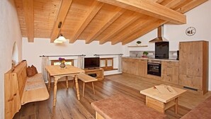 A cozy, open-plan living and dining area with wooden flooring and furniture, a built-in kitchen with modern appliances, and a sloped ceiling with exposed beams. - Ferienwohnung Chiemsee (Bernau am Chiemsee)