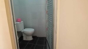 Un baño pequeño y estrecho con un inodoro, una caja de pañuelos rosas y una puerta con contraventanas de metal.