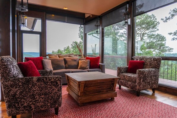Una sala de estar moderna con un sofá, sillones y una mesa de centro. Amplias ventanas ofrecen vistas al exterior.