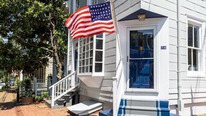 A building with a white exterior, a blue door, and a flagpole with an American flag.