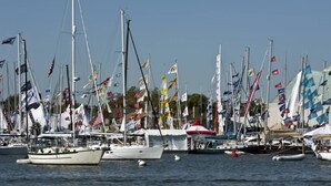 A marina with multiple sailboats docked, flags, and a clear sky.