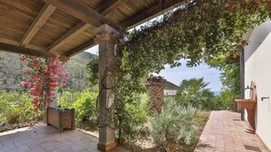 A covered patio area with a stone column, a wooden bench, and a variety of plants and flowers. - RELAIS NISPORTINO - BORGO AI PINI VILLA (Rio dell'Elba)
