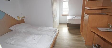A bedroom with a wooden bed, a wooden wardrobe, and a window providing natural light.