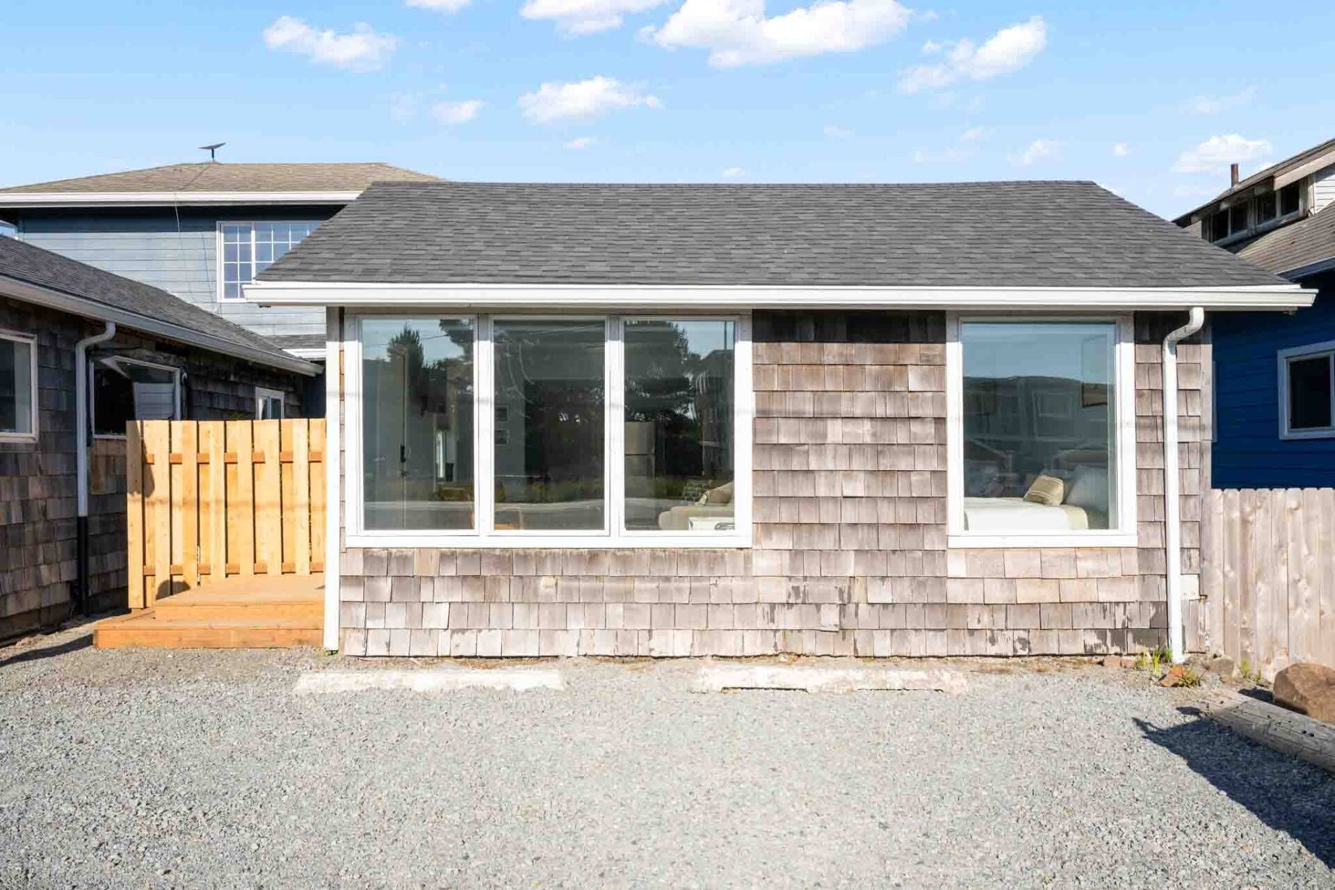 A single-story house with a grey shingle roof, a front porch with a wooden deck, and a large sliding glass door.