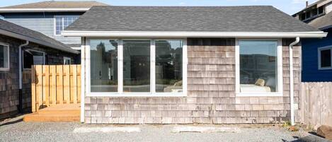 A single-story house with a grey shingle roof, a front porch with a wooden deck, and a large sliding glass door.
