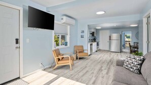 A compact living space with a kitchenette, a sofa, a chair, and a television mounted on the wall.