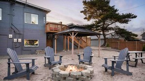 A backyard with a fire pit, four Adirondack chairs, and a wooden deck.