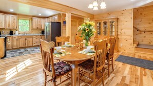 Interior em madeira com mesa de jantar posta para quatro pessoas, rodeada por cadeiras de madeira.