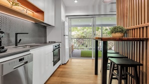 A modern kitchen with white cabinets, a black backsplash, and a wooden dining area with a bench and table. - Bright on the River (Buffalo Apartment 1) (Bright)