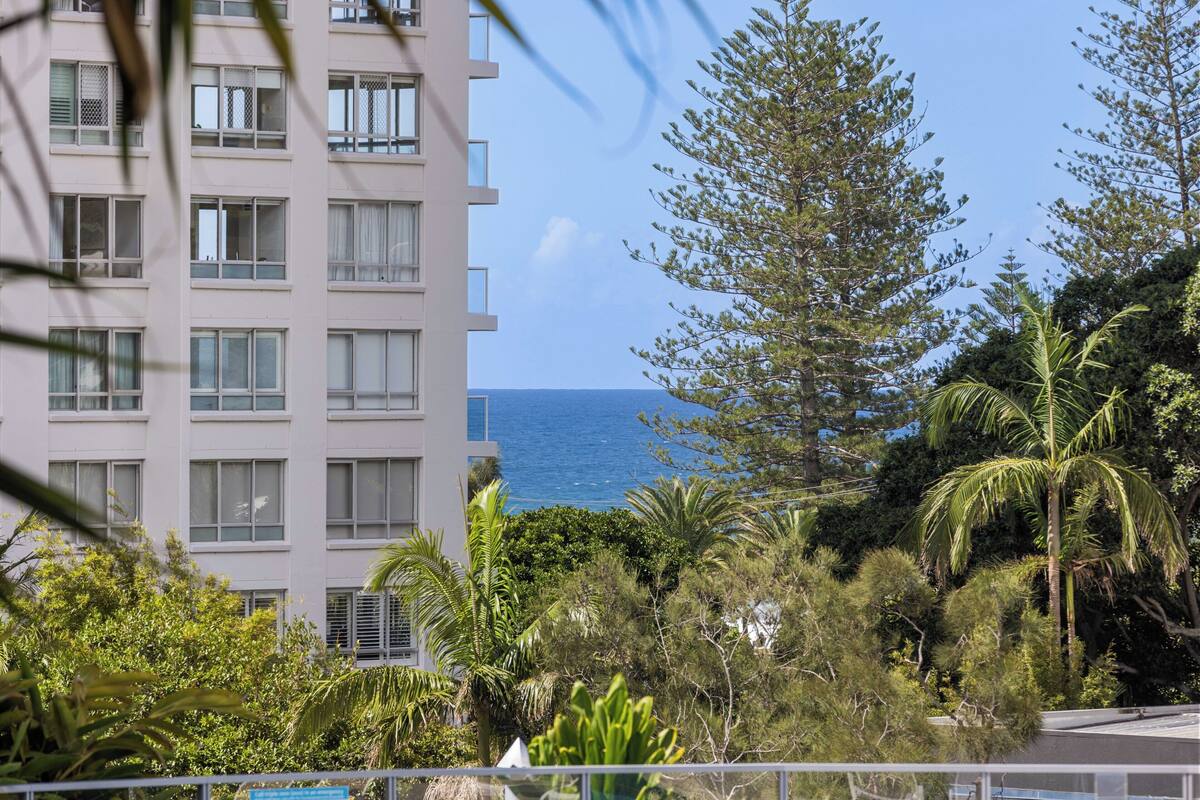 Un edificio de varios pisos con balcones, rodeado de vegetación tropical y vistas al océano.