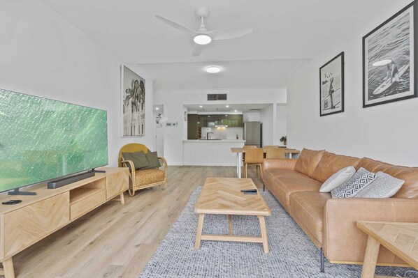 A modern living room with a large flat-screen TV, wooden furniture, a leather sofa, and artwork on the walls.