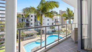 Un balcon avec vue sur une piscine, des palmiers et un ensemble d’immeubles.