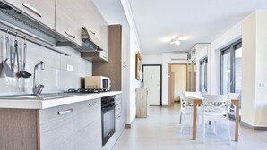 A modern kitchen with a stove, microwave, and cabinets. There is a dining area with a table and chairs. - GuestHost - Sebeto Apartment x3 with Parking & Netfilx (Napoli)