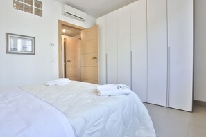 A bedroom with a bed, white curtains, a wardrobe, and an air conditioning unit.