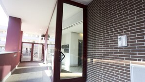 A modern building entrance with a glass door, a metal gate, and a brick wall. - GuestHost - Sebeto Apartment x3 with Parking & Netfilx (Napoli)