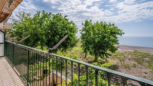 Un balcone con ringhiera in metallo, affacciato su una spiaggia con alberi e cielo sereno.