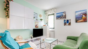 Un soggiorno con televisore, divano, poltrona, tavolo e finestra con tende.