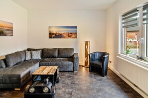 Un salon moderne comprenant un canapé d’angle, une table basse, un fauteuil en cuir noir et une grande fenêtre donnant sur un immeuble.