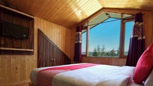 Un dormitorio tipo cabaña de madera con una cama, un televisor montado en la pared y una ventana con cortinas.