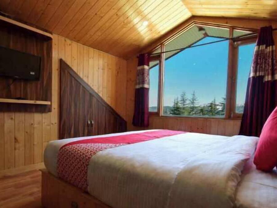 Un dormitorio tipo cabaña de madera con una cama, un televisor montado en la pared y una ventana con cortinas.