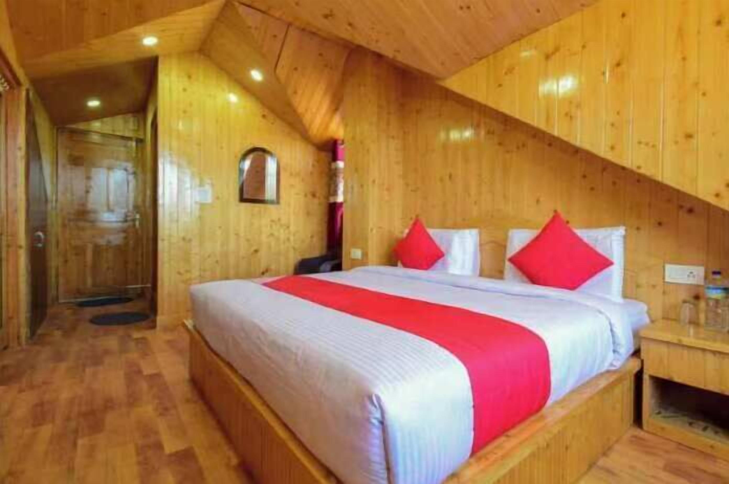 A wooden cabin bedroom with a bed, red pillows, and a nightstand.