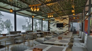 A restaurant with outdoor seating, large windows, and hanging lights. - Castle Glamp by Auroras Resorts (Kosiyakutoli)