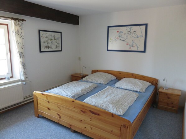 A bedroom with a wooden bed, two bedside tables, a window with curtains, and two framed pictures on the wall.