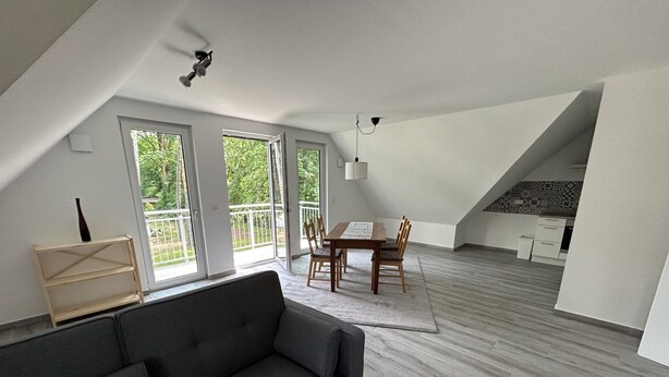 Ein Loft-Zimmer mit einer dunkelgrauen Couch, einem Esstisch mit Stühlen und einer Treppe, die zu einer erhöhten Ebene führt.