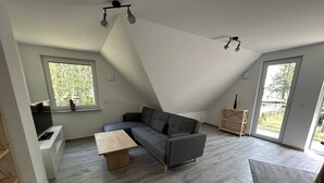 Ein modernes Schlafzimmer im Loft-Stil mit einem großen, grauen Ecksofa, einem Holztisch und einem integrierten Fernseher.