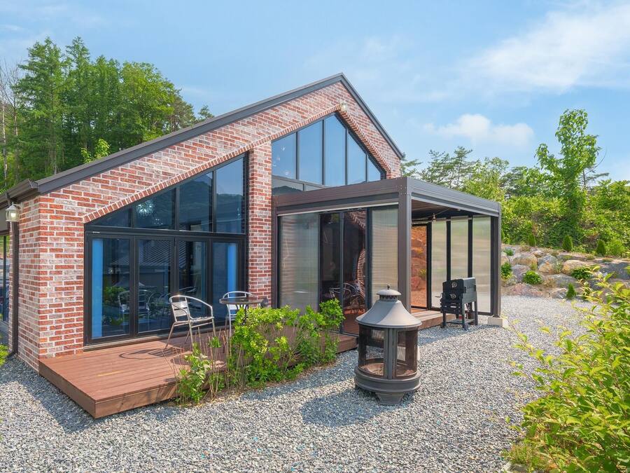 A modern house with a brick exterior, large glass windows, and a deck area with outdoor seating.
