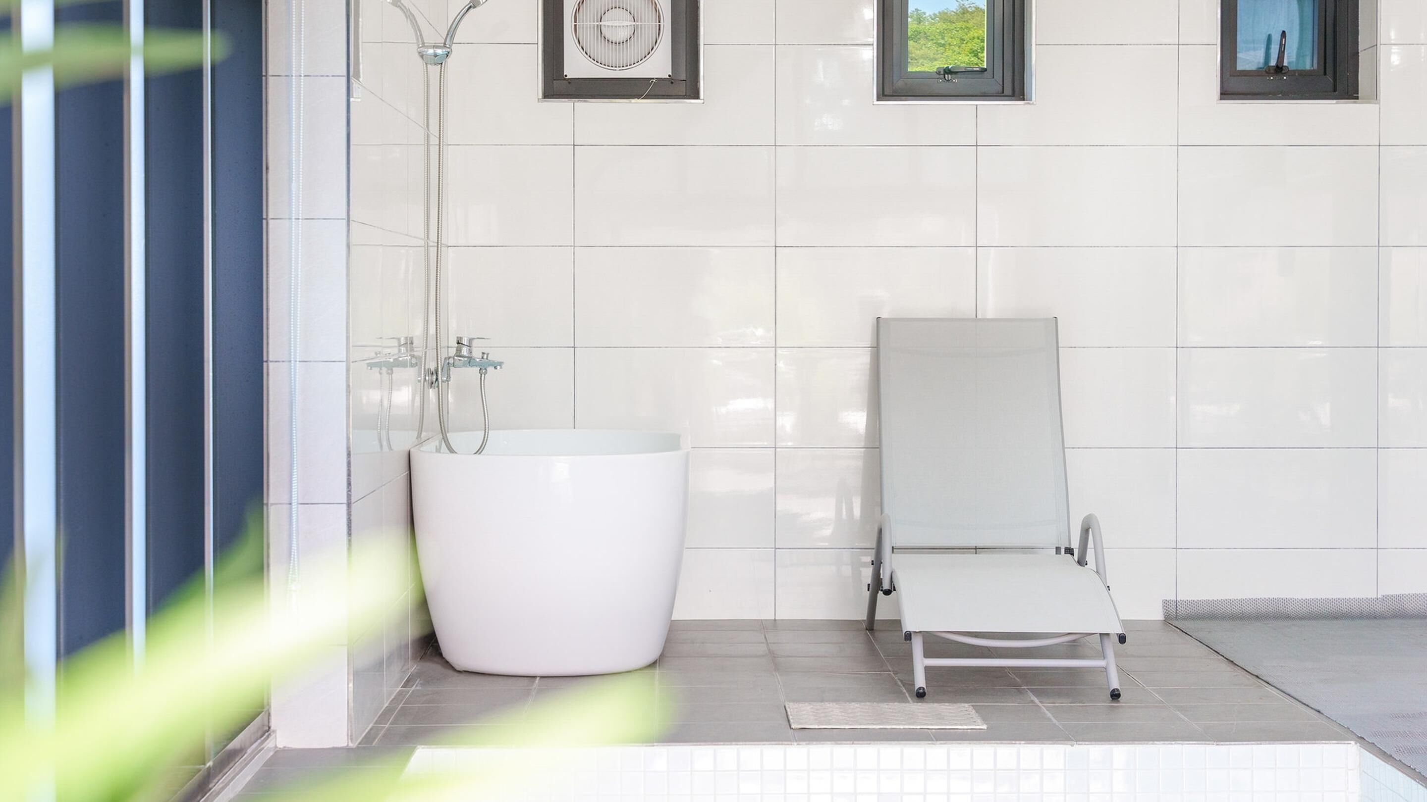 Un baño moderno con una bañera blanca grande, una ducha con cerramiento de vidrio y una pequeña silla blanca.