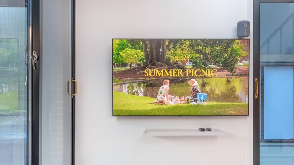 Televisor de pared mostrando una escena de picnic de verano con un estanque, dos personas y una mesa de picnic.