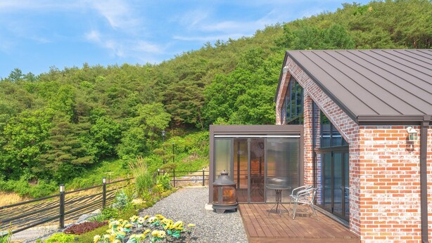 A modern house with a brick exterior, large glass windows, and a deck with outdoor furniture. - Danyang Dandelion Pool Villa (Danyang)