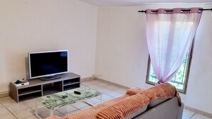 Olohuone, jossa on sohva, televisio ja ikkuna, jossa on läpikuultavat verhot.