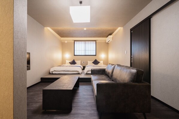 Una habitación de hotel moderna con un sofá, dos camas, una mesa de centro y un ventanal grande.