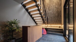 Un escalier moderne avec des marches en bois et une rampe noire, menant à un espace détente doté d’un mur en bois et d’une plante en pot.