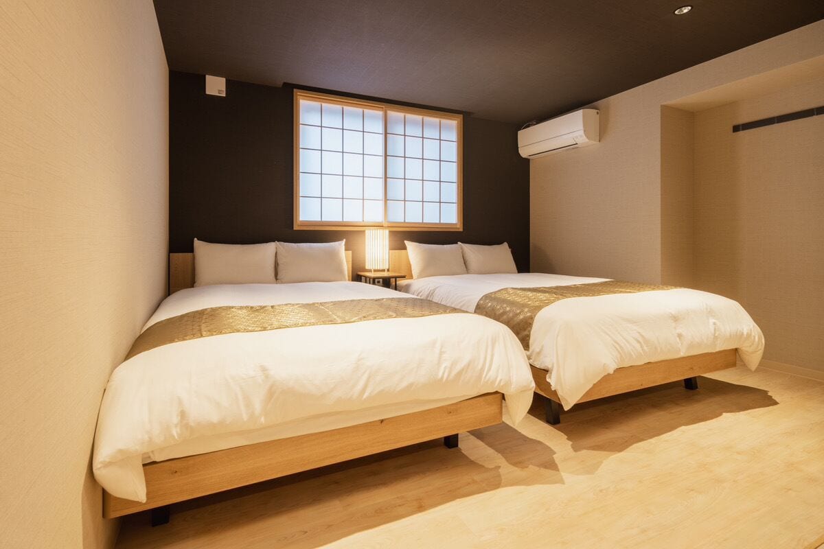 A bedroom with two beds, a large window, and an air conditioning unit.