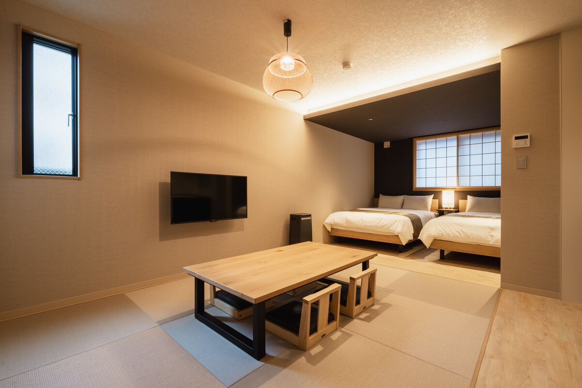 A modern, compact bedroom with a single bed, a small table, a TV, and a window with a view.