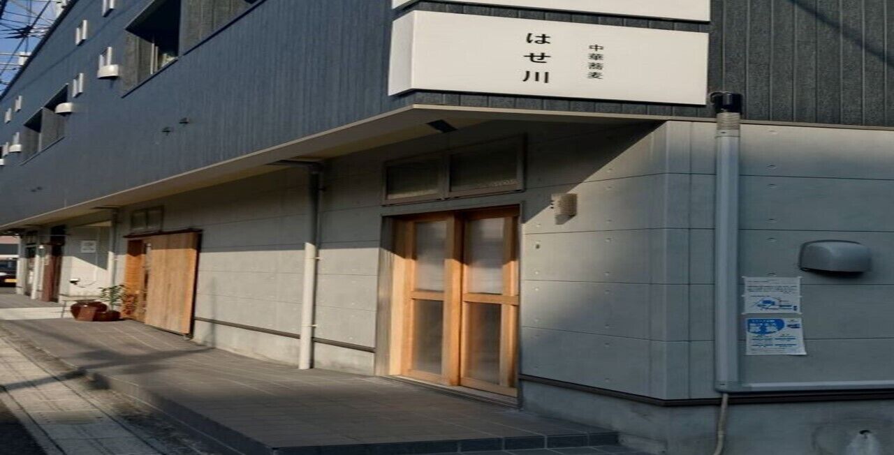 Un edificio con un cartel que dice “はせ川” y una puerta con marco de madera.