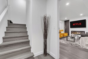 Un salon moderne avec un escalier, une cheminée, un téléviseur à écran plat et un fauteuil jaune.