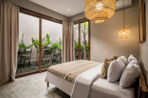 Ein Schlafzimmer mit einem großen Bett, Blick auf Grün hinter Glastüren und einer gewebten Leuchte.