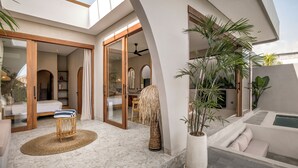 Un interior moderno con tragaluces, una sala de estar con sofá y mesa de centro, un comedor y un pequeño espacio al aire libre con fuente.