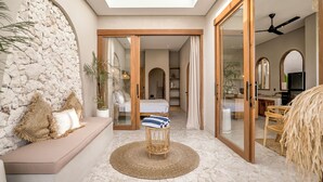 Un espacio habitable amplio con una pared de piedra, un tapete redondo tejido, un banco acolchado y vistas al área de comedor.