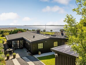 A house with a large deck, a view of the water, and a grassy yard.