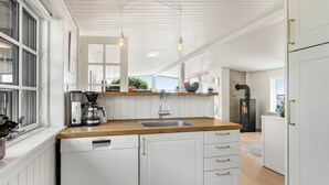 Una cocina moderna con armarios blancos, encimera de madera, lavavajillas integrado e iluminación colgante.