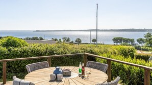 Una terraza de madera con una mesa redonda, sillas y vistas a un cuerpo de agua.